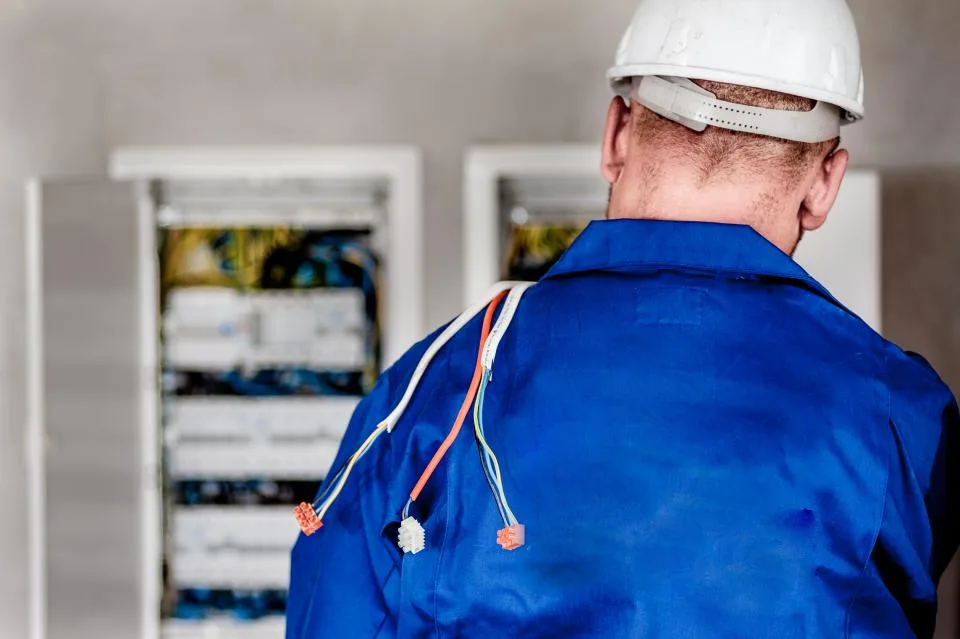 Electrician in a hard hat working at an open breaker panel