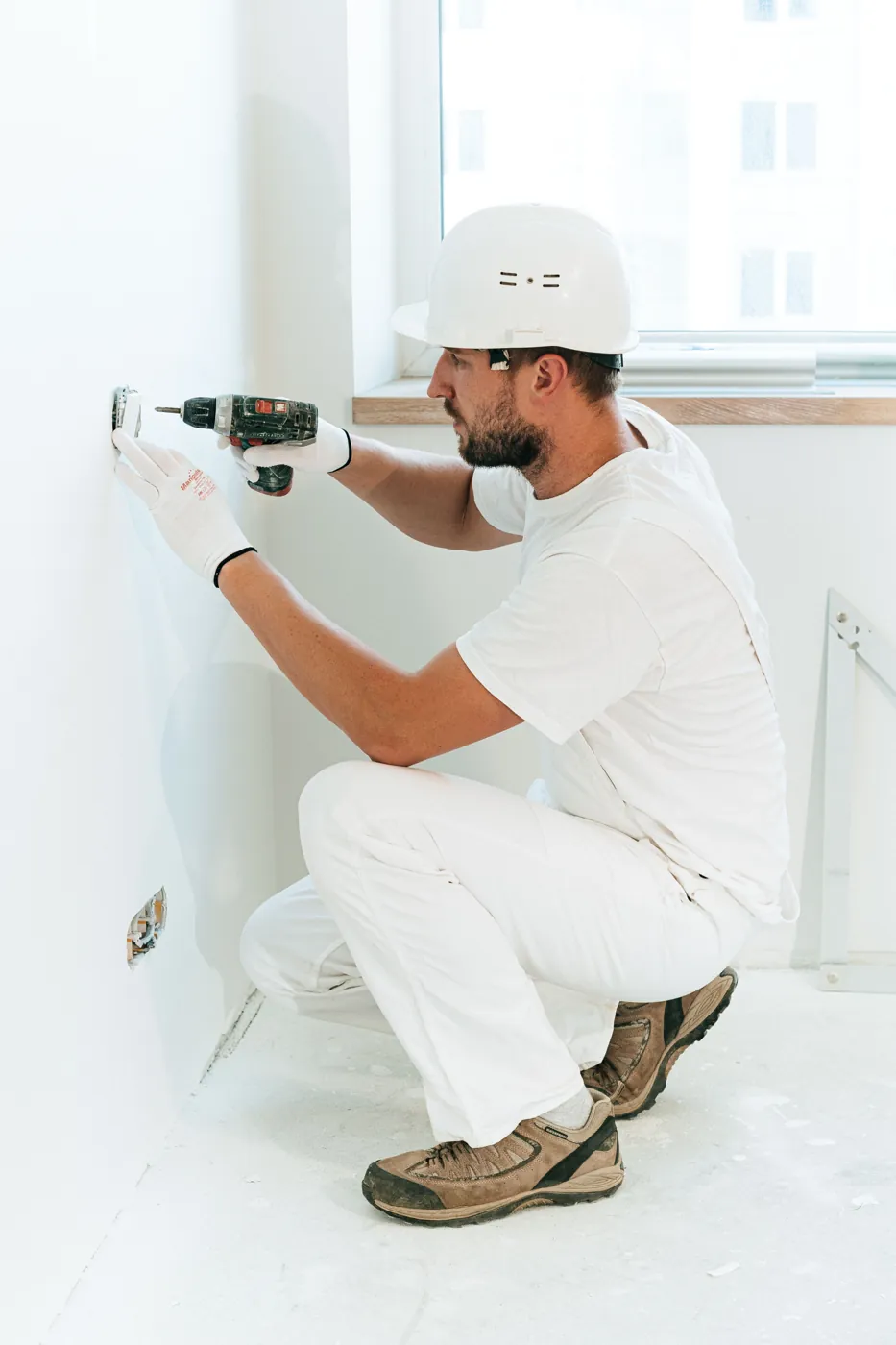 Electrician in a hard hat installing a wall outlet with a cordless drill