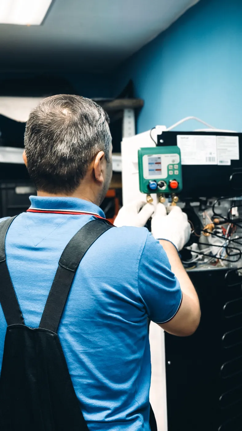 Technician in gloves reading a refrigerant manifold gauge on a cooling unit
