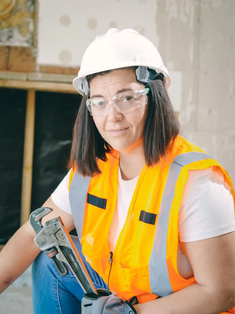 Plumber in a hard hat and safety vest holding a pipe wrench